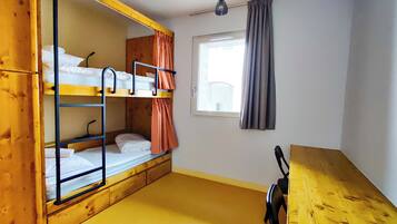 A room with bunk beds, a window with curtains, a wooden table, and a hanging light fixture.
