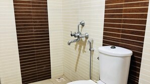 A small bathroom with a toilet, a shower, and a wall with a striped pattern. - 2BHK Apartment near Guruvayur Temple (Guruvayur)