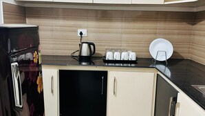 A kitchen with white cabinets, a black refrigerator, a coffee maker, and a plate rack. - 2BHK Apartment near Guruvayur Temple (Guruvayur)