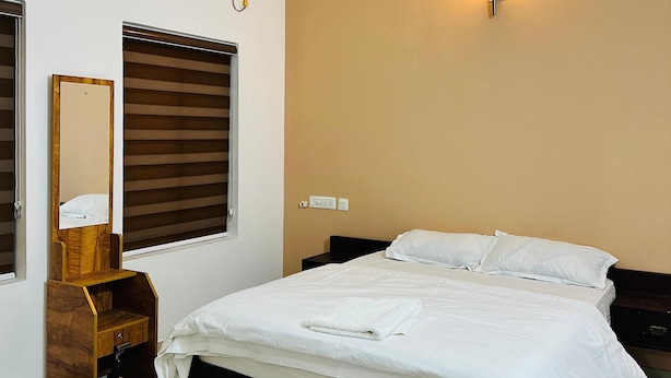 A bedroom with a bed, a ceiling fan, a wall-mounted light, a mirror, and a window with blinds. - 2BHK Apartment near Guruvayur Temple (Guruvayur)