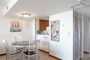 Uma sala de jantar com uma mesa redonda e cadeiras brancas, uma cozinha com armários de madeira e uma porta com painel decorativo.