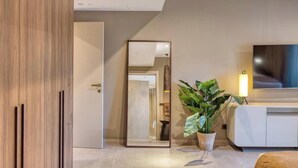 Un salon moderne avec un grand miroir, une plante en pot et un téléviseur à écran plat posé sur un meuble blanc.