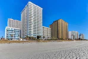 Ein Hotel am Strand mit mehreren Hochhäusern, einem Sandstrand und blauem Himmel.