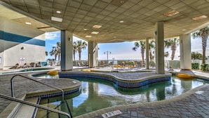 Un espace piscine doté d’une terrasse carrelée, de chaises longues et de palmiers.