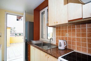 Een keuken met houten kastjes, een roestvrijstalen spoelbak, een koffiezetapparaat en een raam met uitzicht op een balkon.