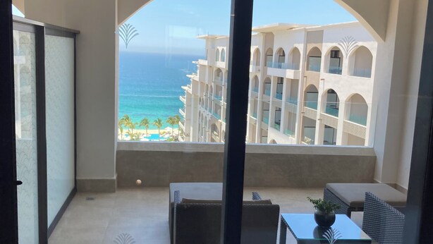 A balcony with a view of the ocean and a building with arches. There are two tables and chairs on the balcony. - Charming 2BR Resort suites in enchanting San José del Cabo tourist Corridor (San José del cabo)