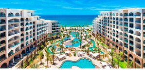 A resort with multiple swimming pools, palm trees, and a view of the ocean. - Charming 2BR Resort suites in enchanting San José del Cabo tourist Corridor (San José del cabo)
