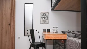 A small room with a wooden floor, a black chair, a wooden desk with a metal frame, a black mug, a white mug, and a framed motivational quote on the wall. - Urban Loft by Neuvel (Athens)
