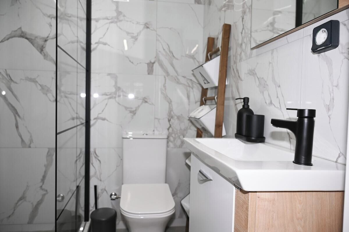 Une salle de bain moderne avec des carreaux de marbre, des toilettes blanches, un lavabo noir et un meuble en bois.