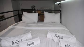 Habitación de hotel con cama, ropa de cama blanca y toallas con la marca 'Neuvel'.