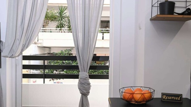 A room with a balcony, grey curtains tied at the center, a small table with a bowl of oranges, and a 'Reserved' sign. - Urban Loft by Neuvel (Athens)