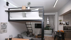 A modern studio apartment with a bunk bed, a sofa, a dining table, and a kitchen area. - Urban Loft by Neuvel (Athens)