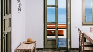 Una habitación con vista al mar a través de un ventanal, una mesa de madera y un sombrero de paja sobre una mesita.