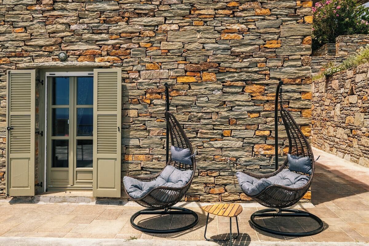 A stone wall with two wicker chairs and a small table in front.