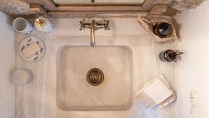 Un lavamanos con grifo dorado, un jabonera, una esponja y una toalla.