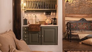 Una habitación acogedora con techo de madera, un mueble verde con utensilios de cocina, un sofá con cojines y una alfombra estampada.