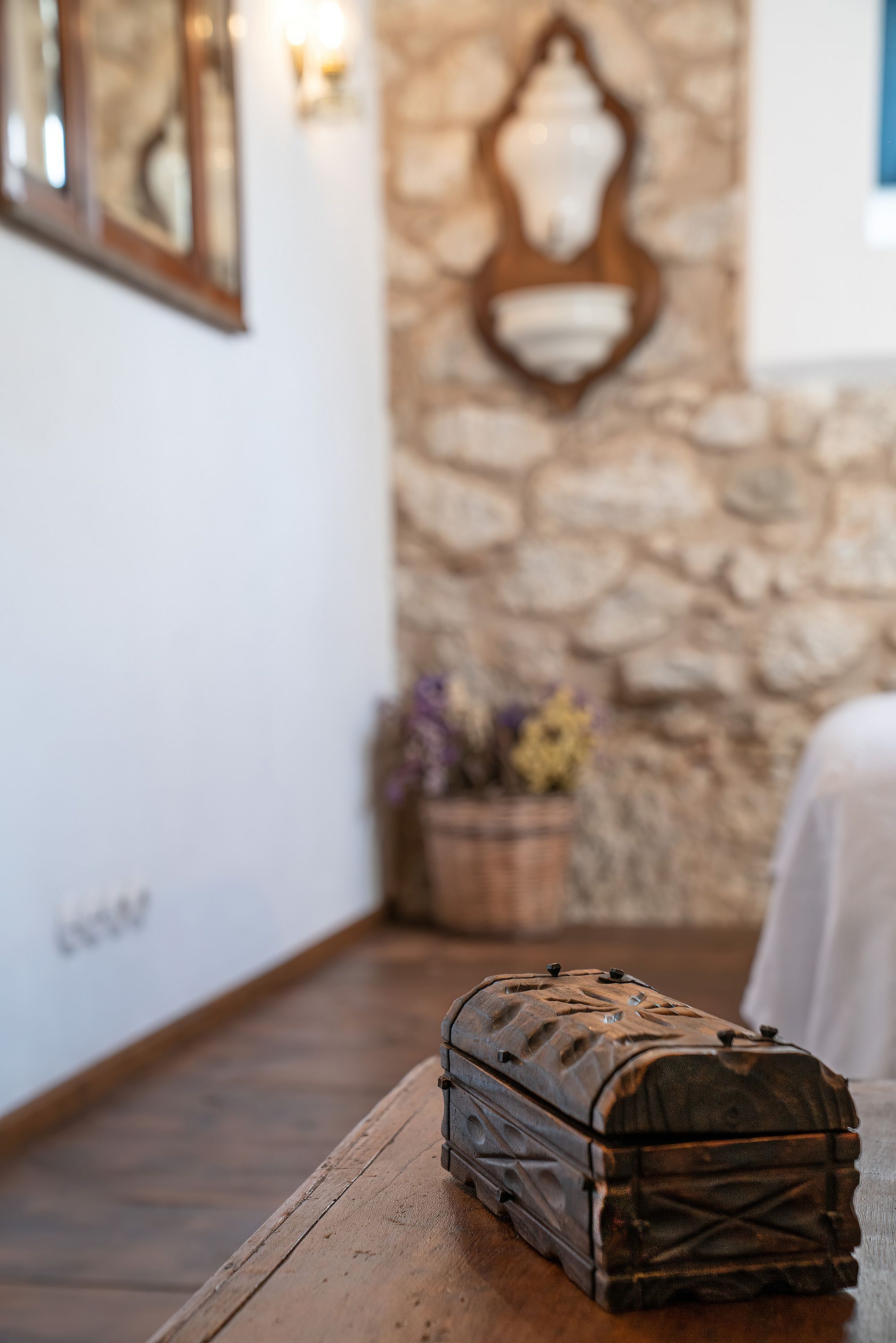 A wooden table with a vintage suitcase. A stone wall and a decorative mirror are in the background.