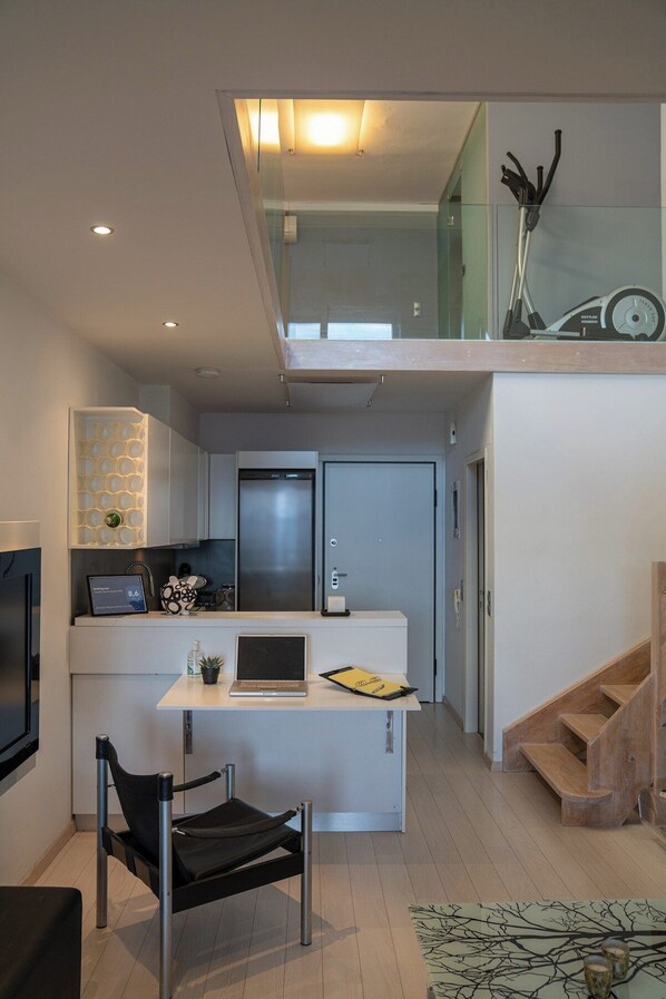 A modern kitchen with a built-in refrigerator, a small dining area with a table and chair, and a staircase leading to an upper level.