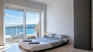 Un dormitorio moderno con una cama grande, vista al mar y un balcón con mobiliario exterior.
