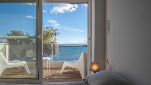 Una habitación con una cama, una mesita de noche, una lámpara y vistas al mar a través de un ventanal.