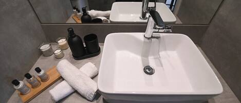 A bathroom with a large white sink, a mirror, and toiletries on a wooden tray.