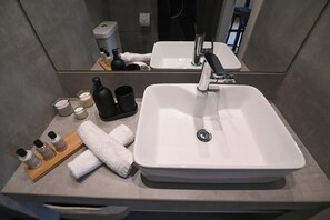Un baño con un lavamanos grande de color blanco, un espejo y artículos de tocador sobre una bandeja de madera.