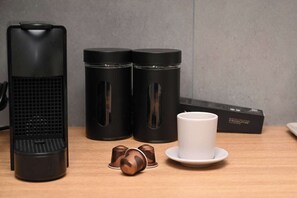 Una cafetera, dos termos negros, una taza blanca y una caja sobre una mesa de madera.
