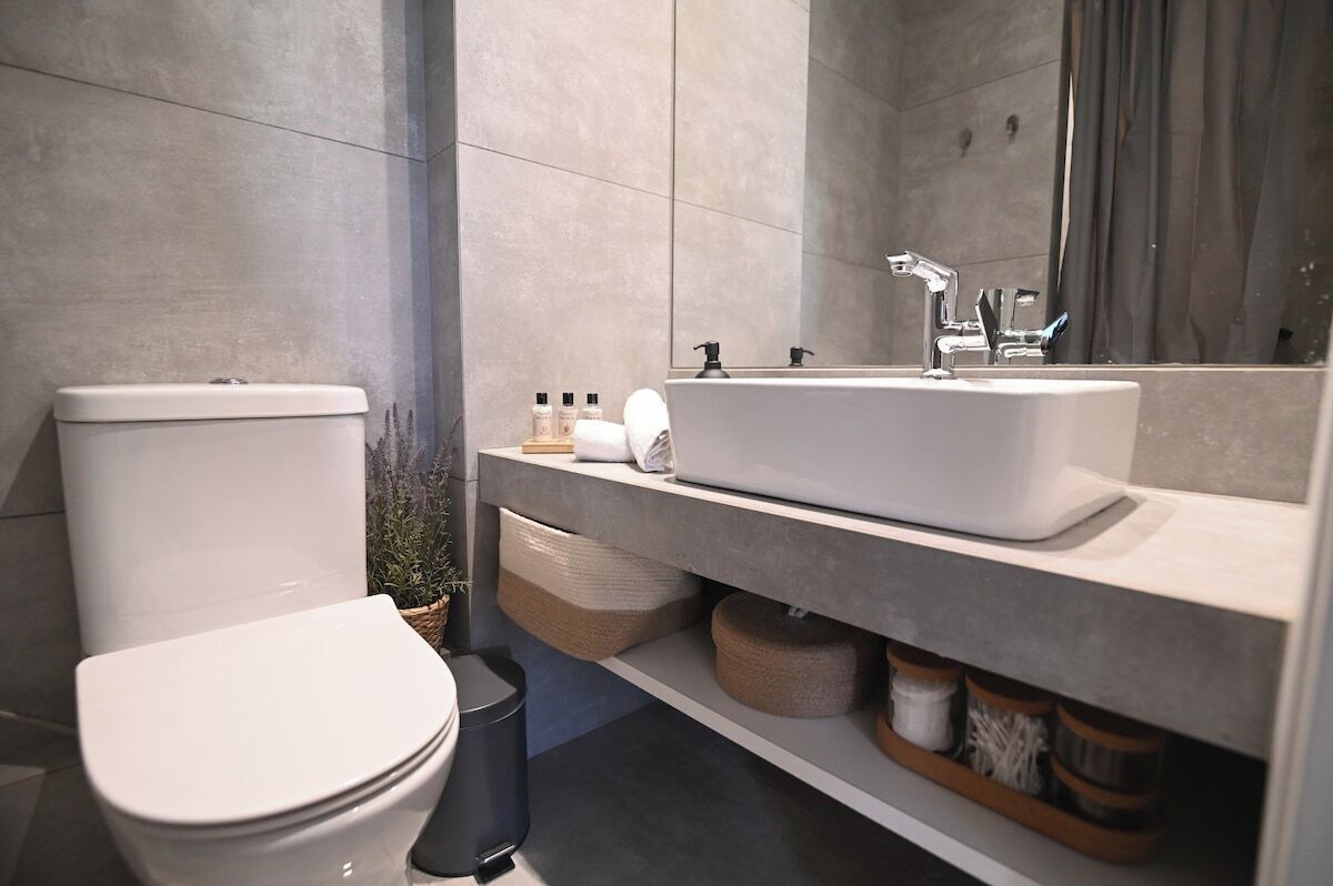 A modern bathroom with a white toilet, a large sink with a mirror above it, and a shelf with toiletries.