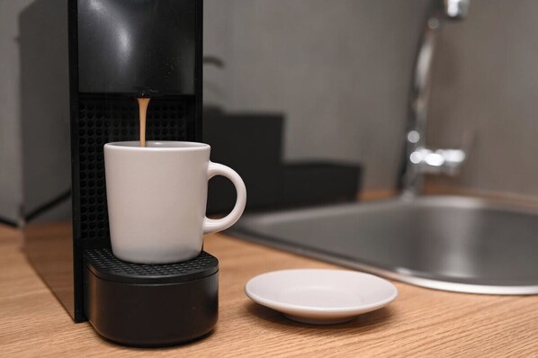 Une machine à café verse du café dans une tasse blanche posée sur un support noir. Un évier et une assiette blanche se trouvent à proximité.