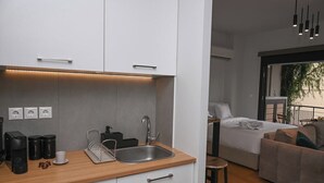 Cucina moderna con piano di lavoro in legno, lavello e macchina per caffè. Si intravede un letto e un balcone sullo sfondo.