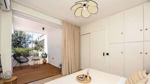 A bedroom with a bed, a bedside table, a chair, and a view of the outdoors. - Coastal Charm by Neuvel (Glyfada)