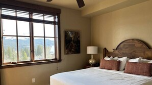 Una camera da letto con un letto grande, un comodino con una lampada, un quadro appeso al muro e una finestra vista montagna.