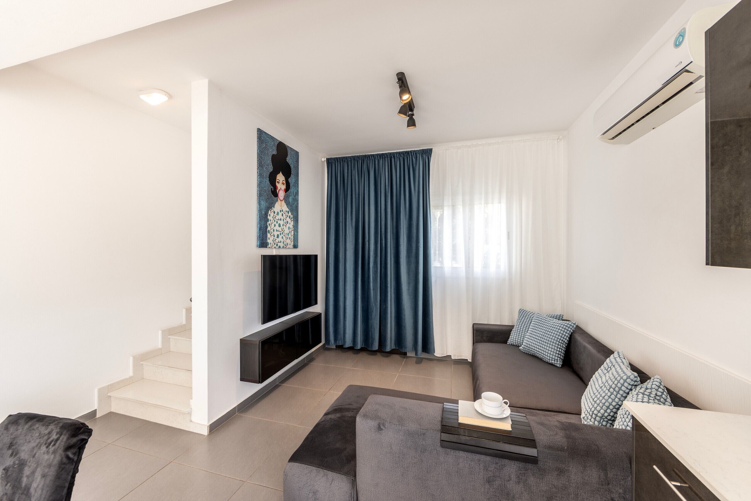 Ein modernes Wohnzimmer mit Sofa, Couchtisch und Fernseher. Eine Treppe führt zu einer weiteren Ebene.