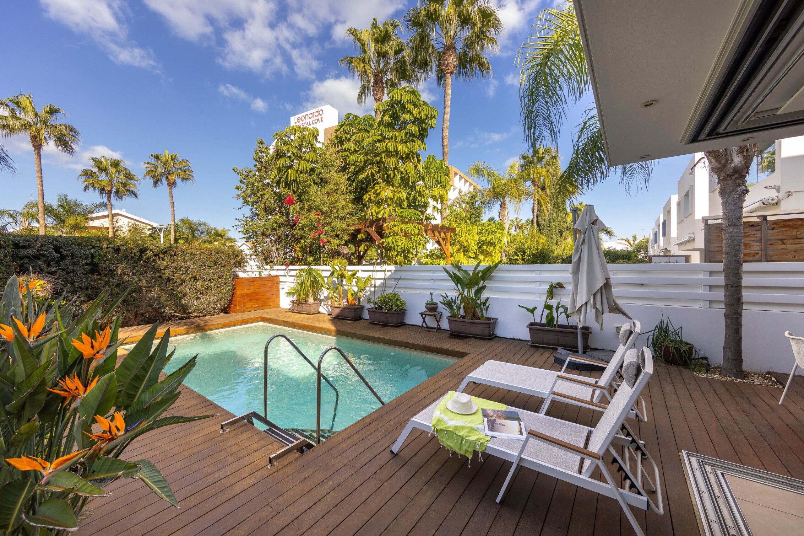 A wooden deck with a pool, lounge chairs, and potted plants.