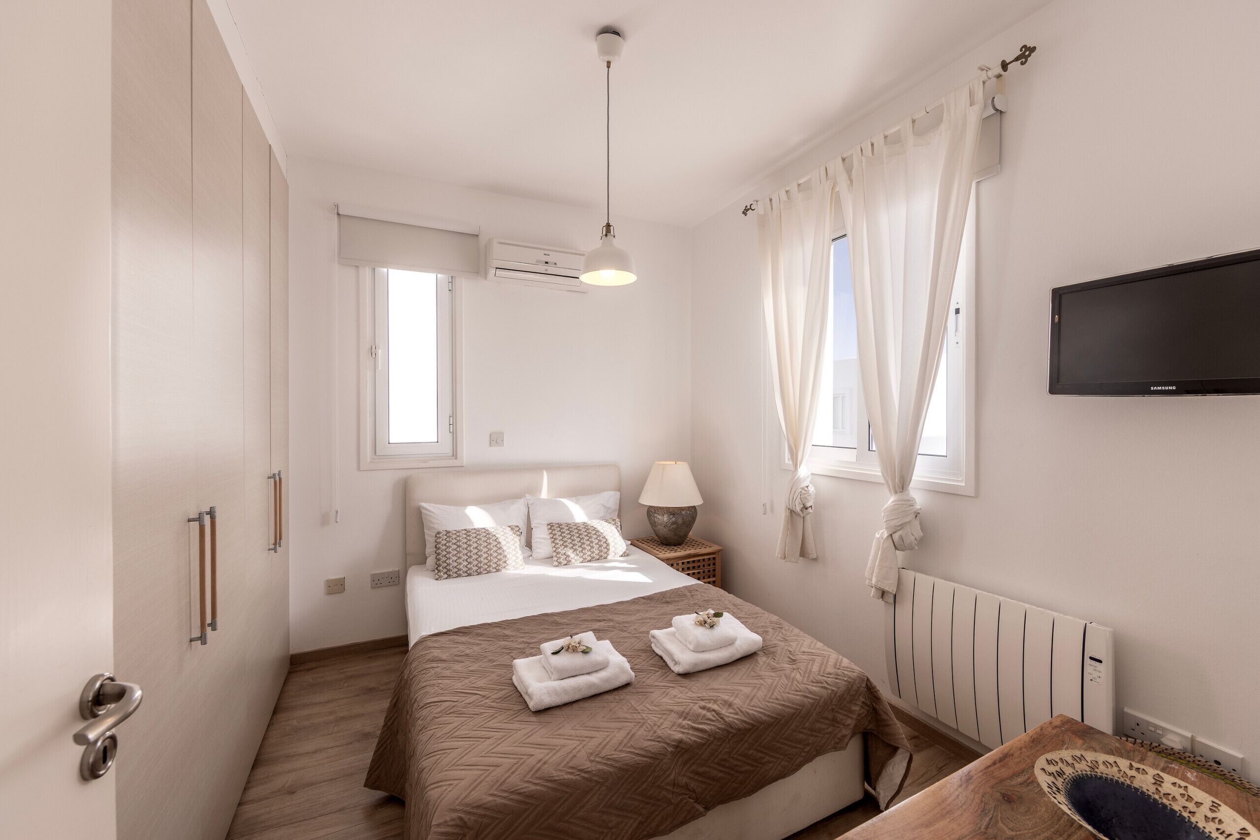 Un dormitorio moderno con cama, lámpara de noche, aire acondicionado y televisor de pantalla plana.
