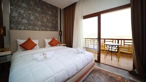 Ein Hotelzimmer mit einem großen Bett, einem Balkon mit Sitzgelegenheiten und Blick auf die Landschaft.