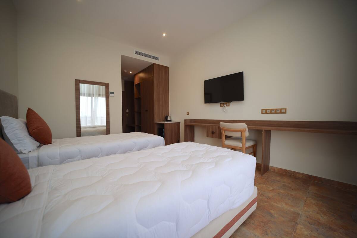 A hotel room with two beds, a desk, a chair, a TV, and a wardrobe.