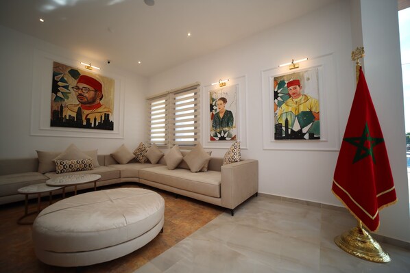 En moderne stue med en beige hjørnesofa, en rund fodsæde og to billeder på væggene.