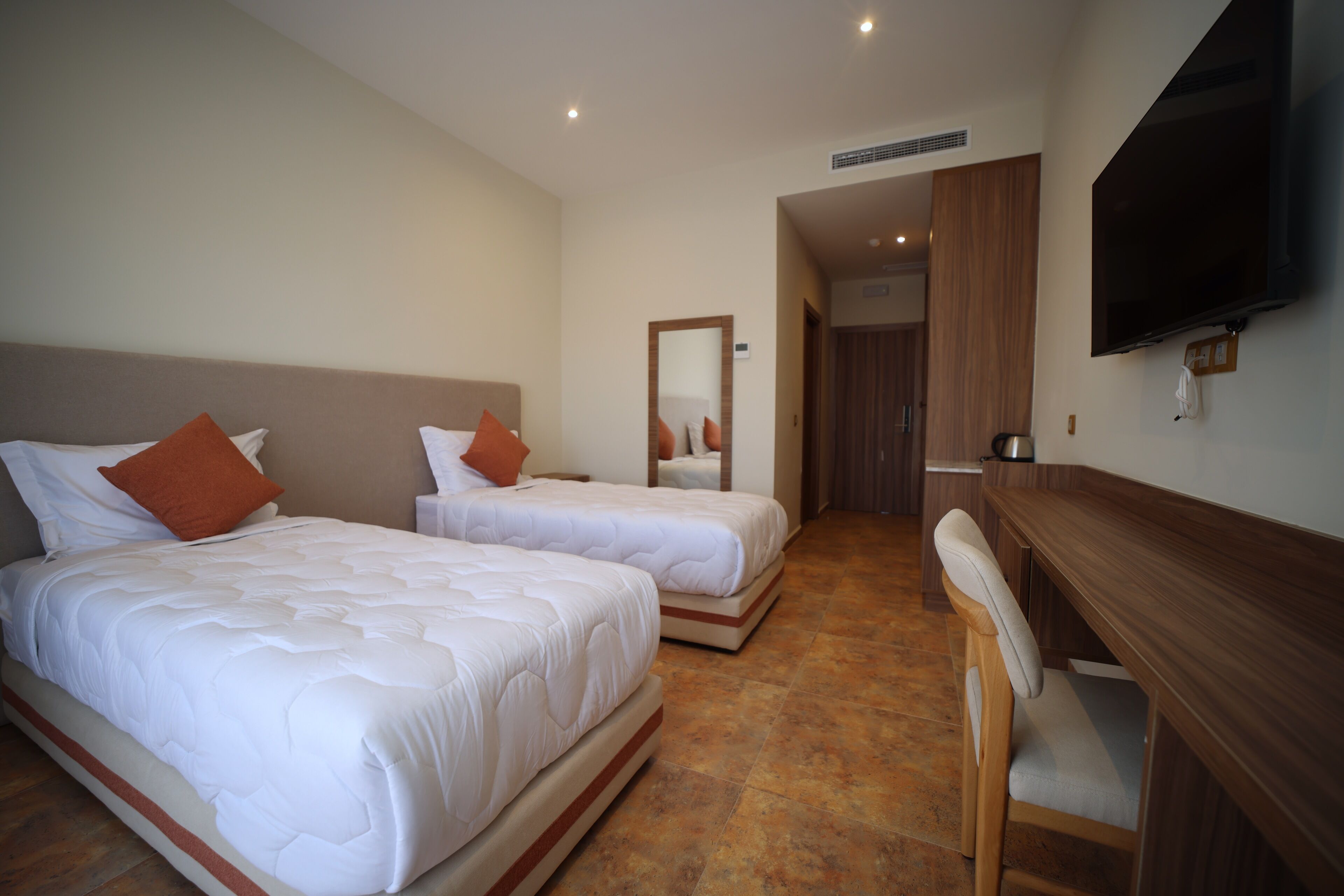 A hotel room with two beds, a desk, a chair, and a TV.