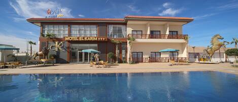A hotel with a swimming pool, a sign reading "Motel El Karim", and a statue of a horse.