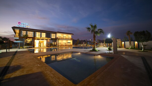 Ein Hotel mit Swimmingpool, Palmen und einer gut beleuchteten Fassade.