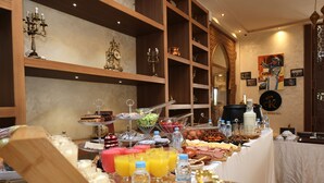 Ein reichhaltiges Buffet mit verschiedenen Speisen und Getränken, Holzregale mit Dekorationsobjekten und eine Wand mit gerahmten Bildern.
