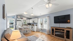 Un salon moderne avec un canapé, une table et une lampe. Il y a un coin cuisine avec des placards et une table à manger. Un téléviseur est fixé au mur.