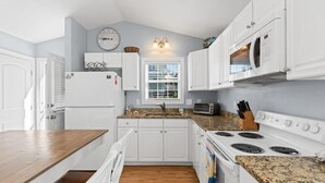 Une cuisine compacte avec des meubles blancs, un four à micro-ondes encastré, une cuisinière et un grille-pain.