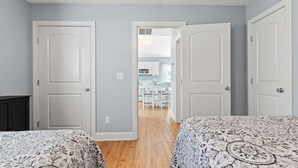 Une chambre avec deux lits, un plancher en bois et une vue sur un coin cuisine.