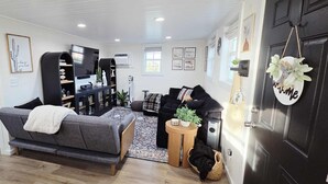 Een moderne woonkamer met een grijze bank, een zwarte fauteuil, een houten bijzettafeltje en een zwarte tv-meubel.