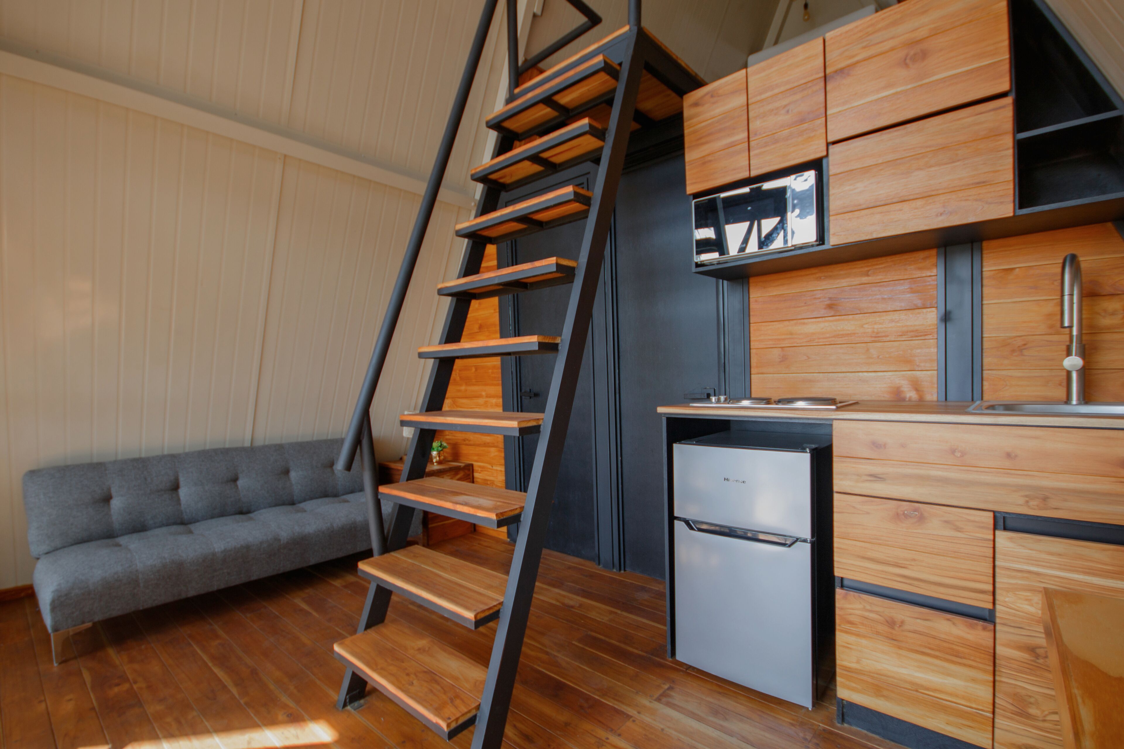 A compact kitchen with wooden cabinets, a built-in refrigerator, and a grey sofa.