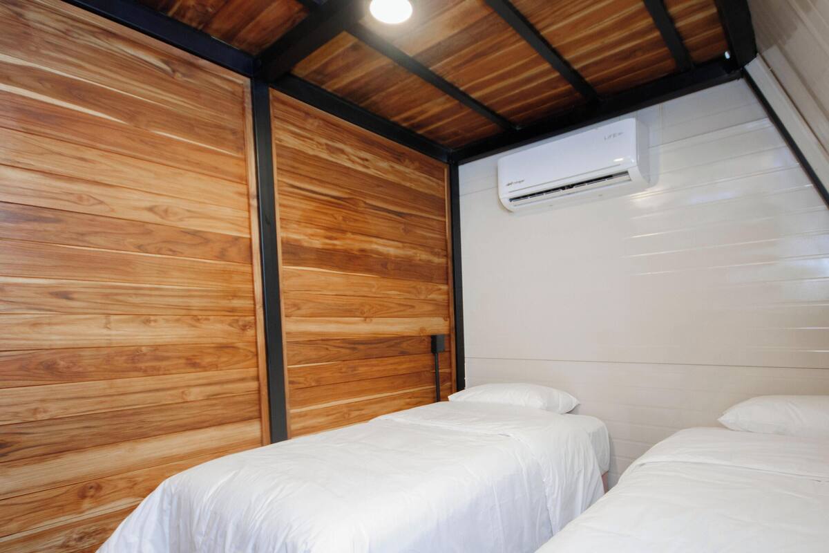 Ein kleiner, kompakter Raum mit zwei Einzelbetten, Holzwandverkleidung und einem Deckenventilator.
