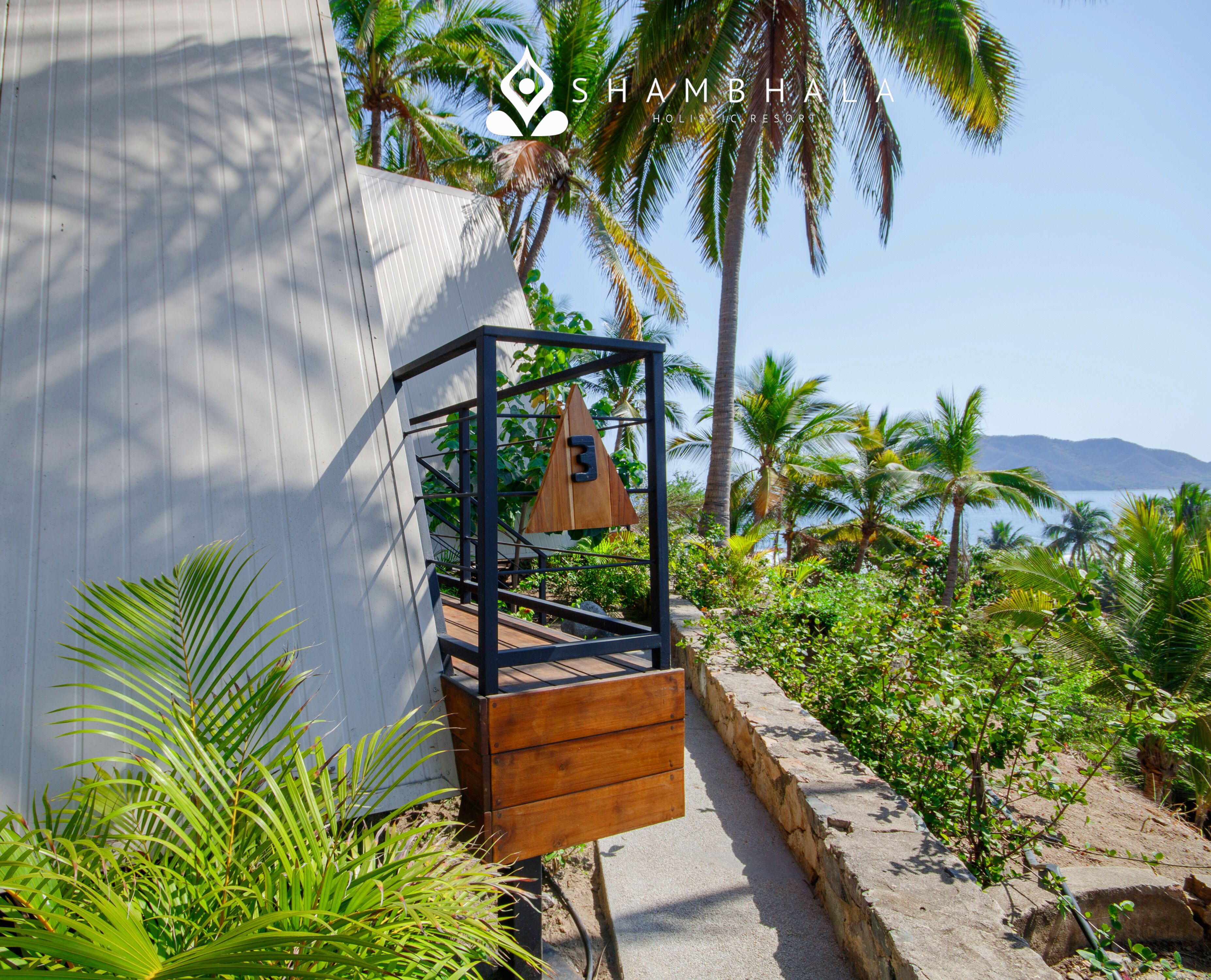 Een houten trap leidt naar een balkon met uitzicht op palmbomen en een berg in de verte.