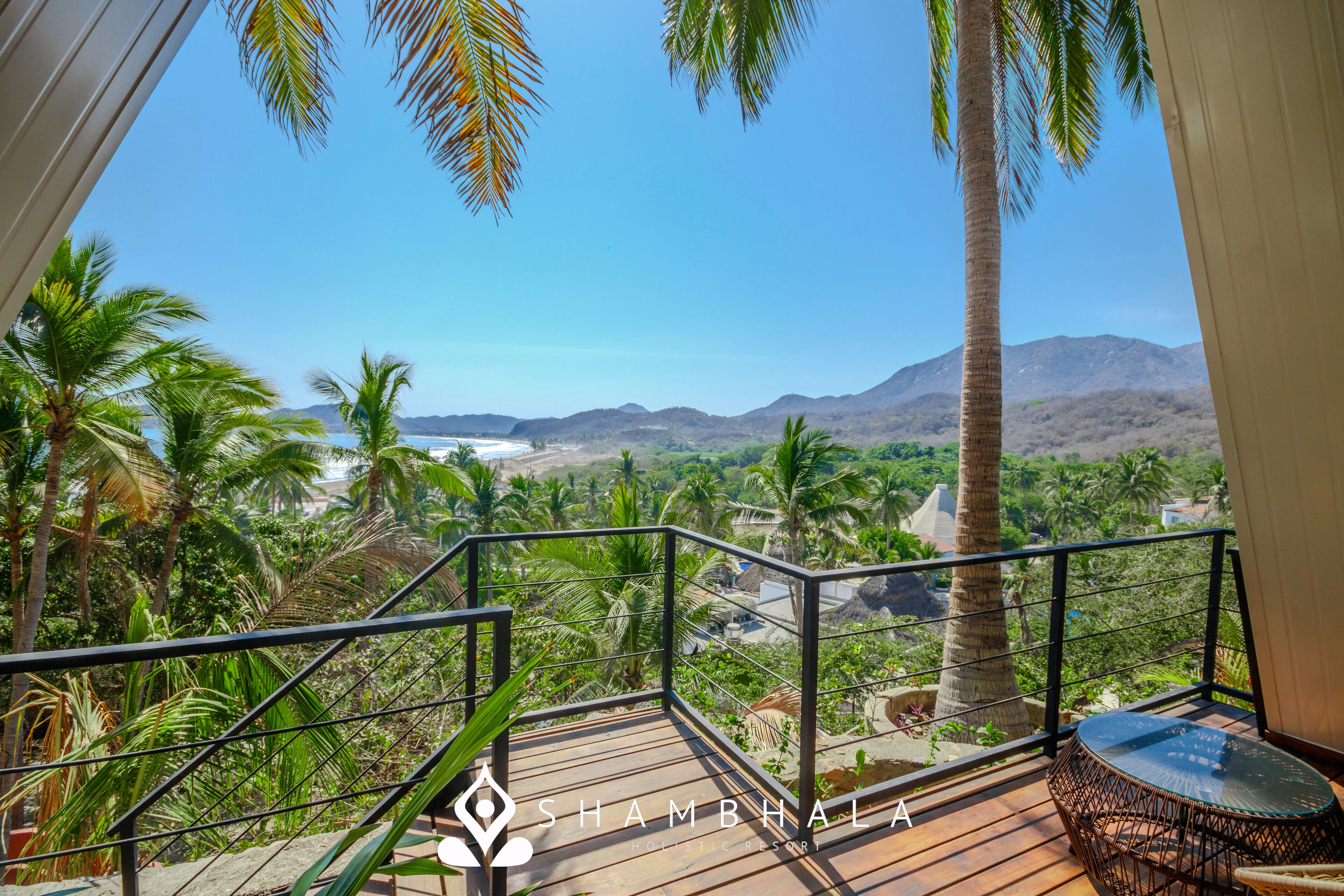 Une terrasse en bois avec une rambarde en métal, d’où l’on peut admirer un paysage tropical avec des palmiers et des montagnes.
